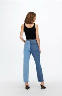 Black tank top paired with high-waisted jeans featuring a two-tone blue design, straight leg, and back pockets. Finished with black heels.