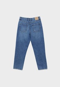 Jean en denim bleu posé à plat montrant le dos avec deux poches et un patch de marque en cuir sur la taille.