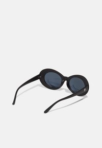 Gafas de sol ovaladas negras con lentes oscuros, acabado mate y varillas curvadas y elegantes. Presentan un pequeño logo en la varilla izquierda.