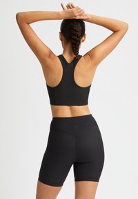 Musta urheilu toppi, jossa on ribattu pinta ja siihen sopivat korkeavyötäröiset shortsit. Mukana urheilutopissa on racerback-malli ja sileä, joustava kangas mukavuutta varten.