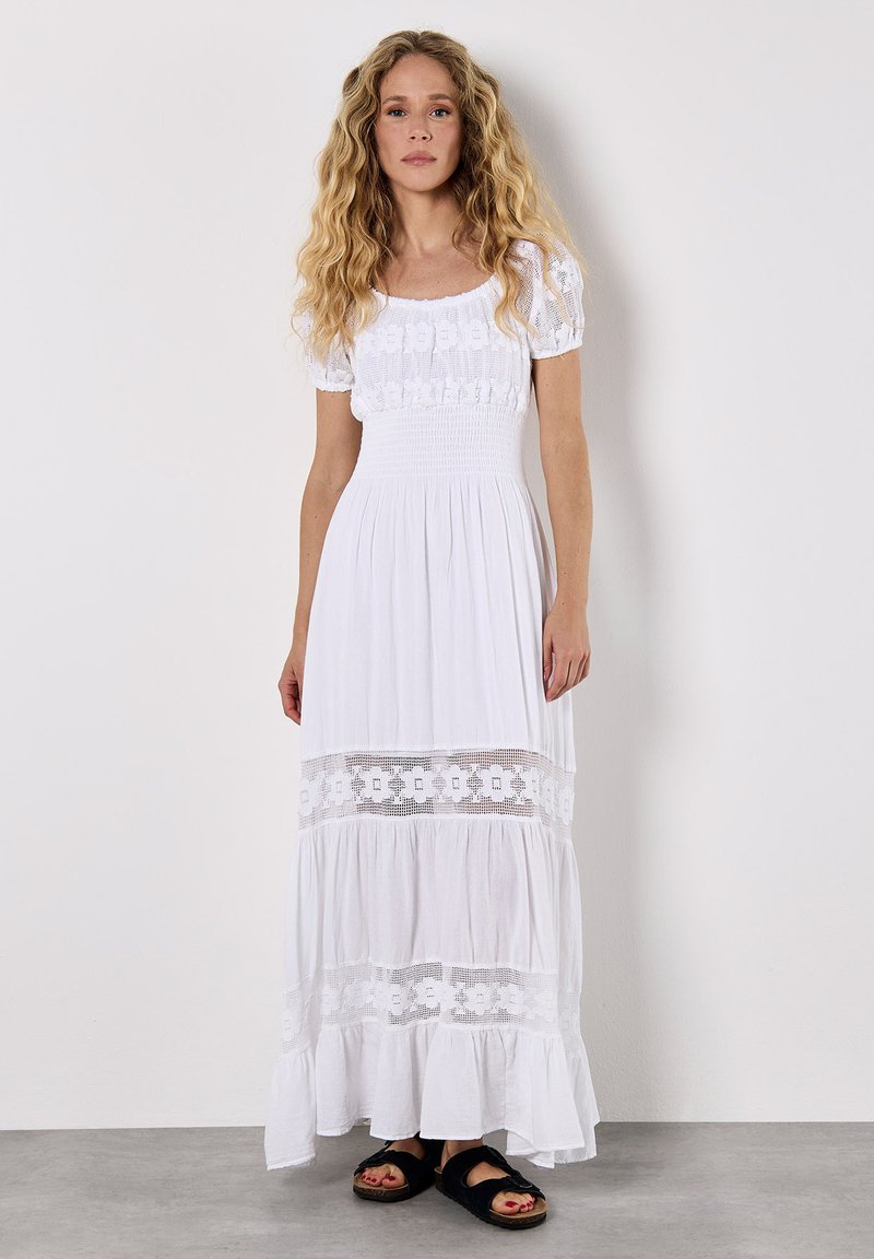 Witte maxi-jurk met puff sleeves, gerimpelde buste, gelaagde gerimpelde zoom en bloemenkantaccenten. Draag met zwarte slide-sandalen.