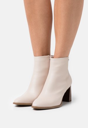 Botines de cuero beige con punta afilada, cierre de cremallera en la parte trasera y tacón grueso con textura similar a la madera.