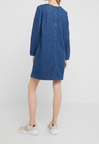 Tummansininen farkkumekko polvipituudella, pitkät hihat, takana vetoketju ja ompeluyksityiskohtia. Yhdistetty vaaleanvärisiin, paksupohjaisiin lenkkareihin.