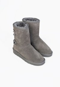 Stivali alti fino al ginocchio in suede grigio con un interno morbido e testurizzato e tre bottoni decorativi laterali. Suola piatta in gomma per stabilità.