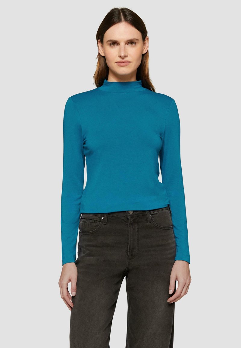 Teal lange mouw top met een hoge halslijn, gemaakt van een gladde stof. Gepaard met donkergrijze broeken met een klassiek vijf-pocket ontwerp.
