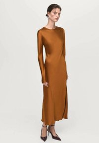 Abito aderente a maniche lunghe in satin marrone ricco, con scollatura rotonda e spacco sull'orlo, abbinato a décolleté a punta color bordeaux.