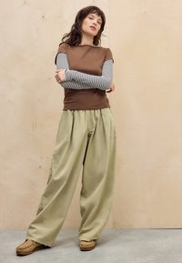Bruine korte mouwen top over een grijs gestreepte lange mouwen shirt, gecombineerd met losse khaki wijde-broeks en lichtbruine schoenen.