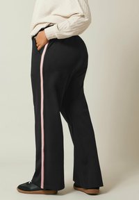 Svarta sweatpants med vida ben, har rosa sidostrikar. Tillverkade av mjukt material, med sidofickor och en avslappnad passform.