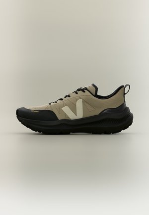 Side view of beige and black off-road sneaker with thick sole and black laces on neutral background.