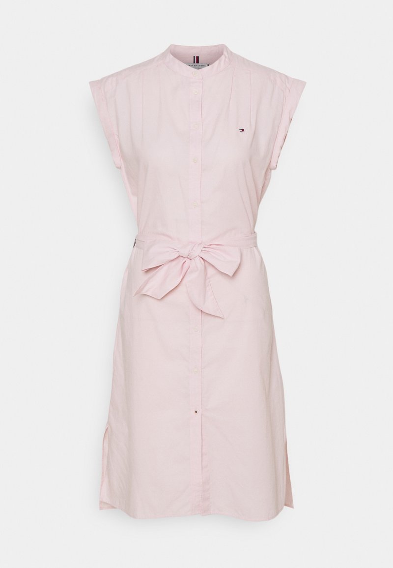 Robe chemise sans manches rose clair avec des boutons sur le devant et une ceinture nouée à la taille, avec un petit logo sur la poitrine.