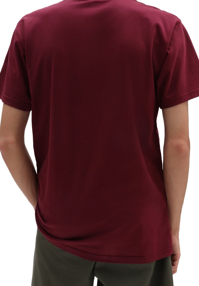 Personne portant un t-shirt bordeaux uni à manches courtes et un pantalon sombre, vue de dos avec les mains reposant le long du corps.