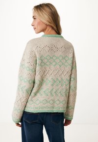 Stickad tröja i ljusbeige med gröna geometriska mönster. Har rund halsringning och lös passform. Texturerad tyg med öppet hantverk.