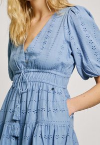 Jasnoniebieska sukienka z bufkami na rękawach, dekoltem w serek, haftowanymi wzorami, elastyczną talią z sznurkiem oraz kieszeniami. Miękka faktura materiału.