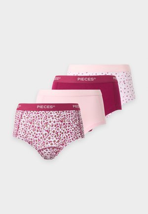 Kvinde iført en beige cropped tanktop og bordeaux farvet højtkilede underbukser, stående barfodet mod en ensfarvet lys baggrund.