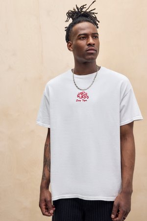 White cotton t-shirt featuring a red embroidered "Easy Tiger" graphic. Short sleeves and a relaxed fit. Model wears a silver chain necklace.