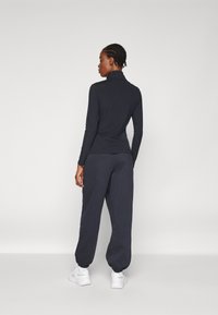 Schwarzes Langarm-Turtleneck-Oberteil kombiniert mit navyblauen Jogginghosen. Weicher Stoff, schlanker Schnitt und schmal zulaufende Bündchen. Weiße Sportschuhe runden das Outfit ab.