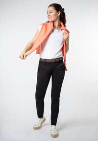 Casual outfit met een wit T-shirt, zwarte slim-fit broek, een koraalkleurige sjaal over de schouders gedrapeerd, en witte sneakers met tekstuur op de zolen.