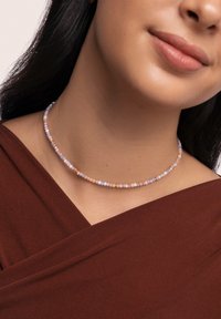 Perlenchoker-Halskette mit pastellfarbenen runden Perlen und kleinen goldenen Akzenten, getragen um den Hals, vor einem braunen Stoffhintergrund.