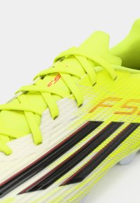 Κίτρινο ποδοσφαιρικό παπούτσι με υφή στην επιφάνεια, μαύρες και κόκκινες λεπτομέρειες και κορδόνια. Ελαφρύ με αεροδυναμικό σχήμα.