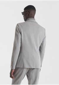 Blazer ajustado de color gris claro, con cierre de un solo botón, solapas con muesca, dos aberturas traseras y cuello texturizado, combinado con pantalones a juego.