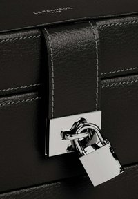Borsa nera in pelle con una prominente chiusura a lucchetto argentato, con cuciture argentate a contrasto e logo del brand embossato sulla parte superiore.