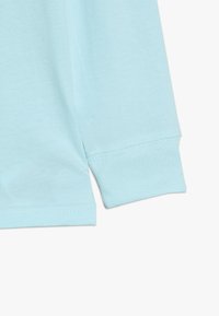 Ljust blå långärmad skjorta i mjukt bomullsmaterial, med en sömlös manschett och ren sömnad längs nederkanten och ärmkanterna.