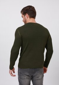 Suéter acanalado de color verde oliva con mangas largas, cuello redondo y tejido texturizado. La vista trasera muestra un diseño ajustado con ligeras aberturas laterales.