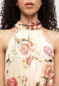 Φωτεινό λουλουδένιο φόρεμα με κρεμ φόντο, τριαντάφυλλα σε ροζ και λευκό, ρεβέρ ύφασμα και σχέδιο με δέσιμο στο λαιμό.