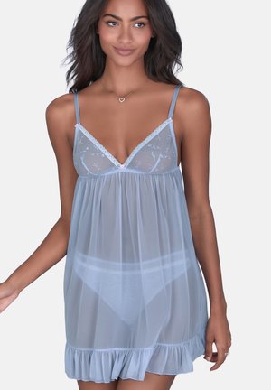 Woman wearing sheer light blue lingerie slip with floral embroidery and ruffled hem, posing against plain background.