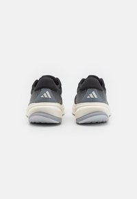 Des chaussures de sport en mesh grises avec une semelle intermédiaire blanche et une semelle extérieure grise, arborant des accents noirs sur le dessus et un logo à trois rayures sur le talon.
