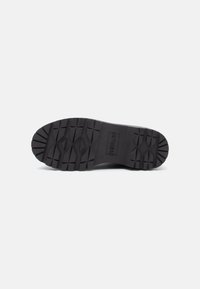 Suela de zapato de goma negra con patrones de relieve profundos y el nombre de la marca "REPLAY" estampado en el centro sobre un fondo blanco.