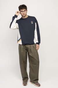 Navy and white sweatshirt with a logo, paired with olive-green trousers. Features a relaxed fit and geometric design accents.