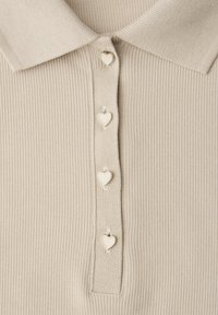 Chemise beige à col côtelé avec une patte de boutonnage comportant quatre boutons crème en forme de cœur disposés en ligne verticale.