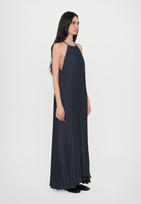 Abito maxi plissettato di un blu scuro con scollatura a halter, caratterizzato da tagli laterali e un materiale fluido che scende fino al pavimento.