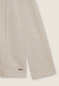 Tessuto beige chiaro a coste con una morbida texture. Presenta un piccolo etichetta logo marrone vicino all'orlo. Design semplice e classico.