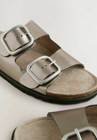 Metalliska silver sandaler som har två breda remmar med stora silver spännen, en mockaliknande fotbädd och en svart gummisula.