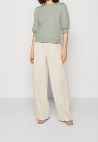 Lys grøn pullover med puffede ærmer, parret med brede, beige linnedbukser. Tekstureret stof og afslappet pasform. Neutrale nuancer skaber et blødt udseende.