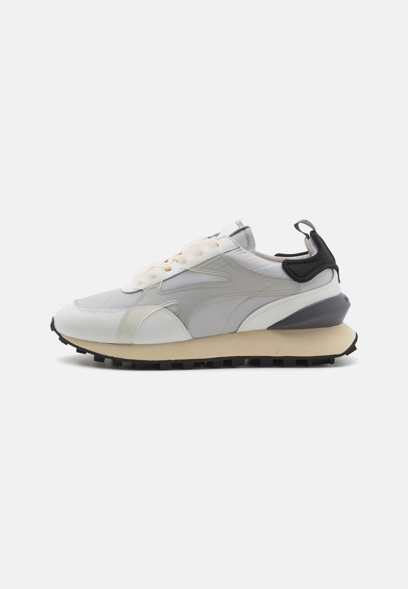 Sneaker with a mixed material upper in light gray, white, and black accents. Features a chunky sole with textured tread and lacing system.