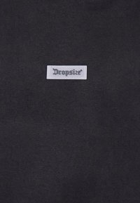 Tissu noir à la texture lisse avec une étiquette rectangulaire blanche portant l'inscription "Dropsize®" en lettres gris foncé.
