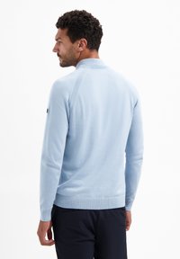 Lichtblauwe trui met een geribde kraag en manchetten, voorzien van een zachte textuur en slim fit. Opvallend detail: zwart logo op de linker mouw.