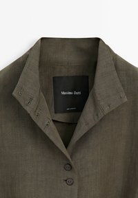 Olivgrön linsskjorta med krage, knappslå och fem knappar. Lappen visar "Massimo Dutti", vilket indikerar märket.