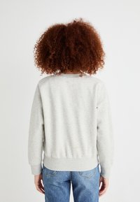 Sweatshirt gris avec un col rond, des poignets et une taille côtelés ; présente une coupe décontractée et ample. Porté avec un jean bleu.
