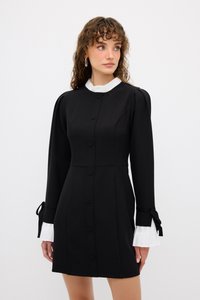 Musta mekko, jossa onvaroitetu siluetti, napit edessä, pitkät hihat valkoisilla hihoilla ja nauha koristeita ranteissa.