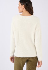 Suéter blanco de felpa con un escote amplio y mangas largas, que presenta una textura suave. Combinado con pantalones de pana en color verde oliva.