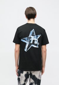 Juoda medvilninė marškinėlių su dideliu mėlynos spalvos ledo žvaigždės piešiniu nugaroje. Trumpomis rankovėmis ir klasikiniu apvaliu kaklu.