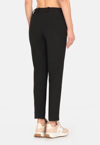 Pantaloni neri su misura con vestibilità dritta, dotati di cintura, tasche laterali e una texture liscia. Indossati con sneakers beige.