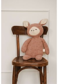 Brązowa pluszowa zabawka króliczek z beżowymi akcentami, okrągłą twarzą, dużymi uszami i teksturowanym ciałem, spoczywająca na drewnianym krześle.