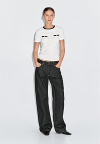 Witte t-shirt met korte mouwen en zwarte rand, voorzien van twee zwarte zakaccenten, gecombineerd met hoge taille donkerdenim wijde broek.