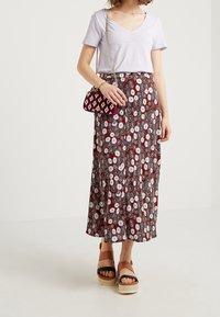 Lila t-shirt med V-ringning kombinerad med en lång morotsröd kjol med vita och svarta blommönster. Chunkiga bruna platåsandaler och en liten väska.