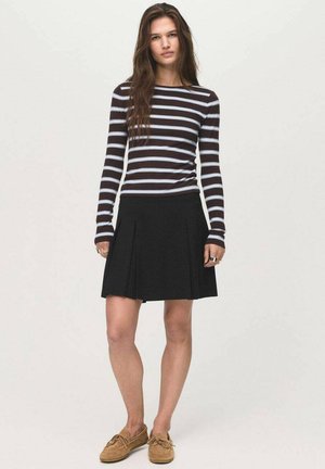 Jupe plissée noire associée à un haut à manches longues rayé avec des rayures marron et bleu clair. Modèle portant des chaussures décontractées.